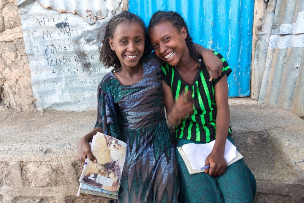 Two young girls laugh together on the steps of their schoolhouse